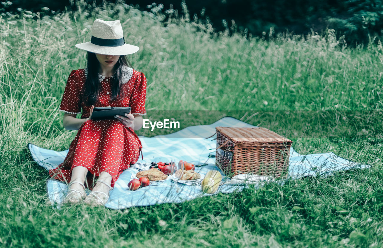 A beautiful young caucasian girl in a red dress sits on a blue bedspread and reads an e-book