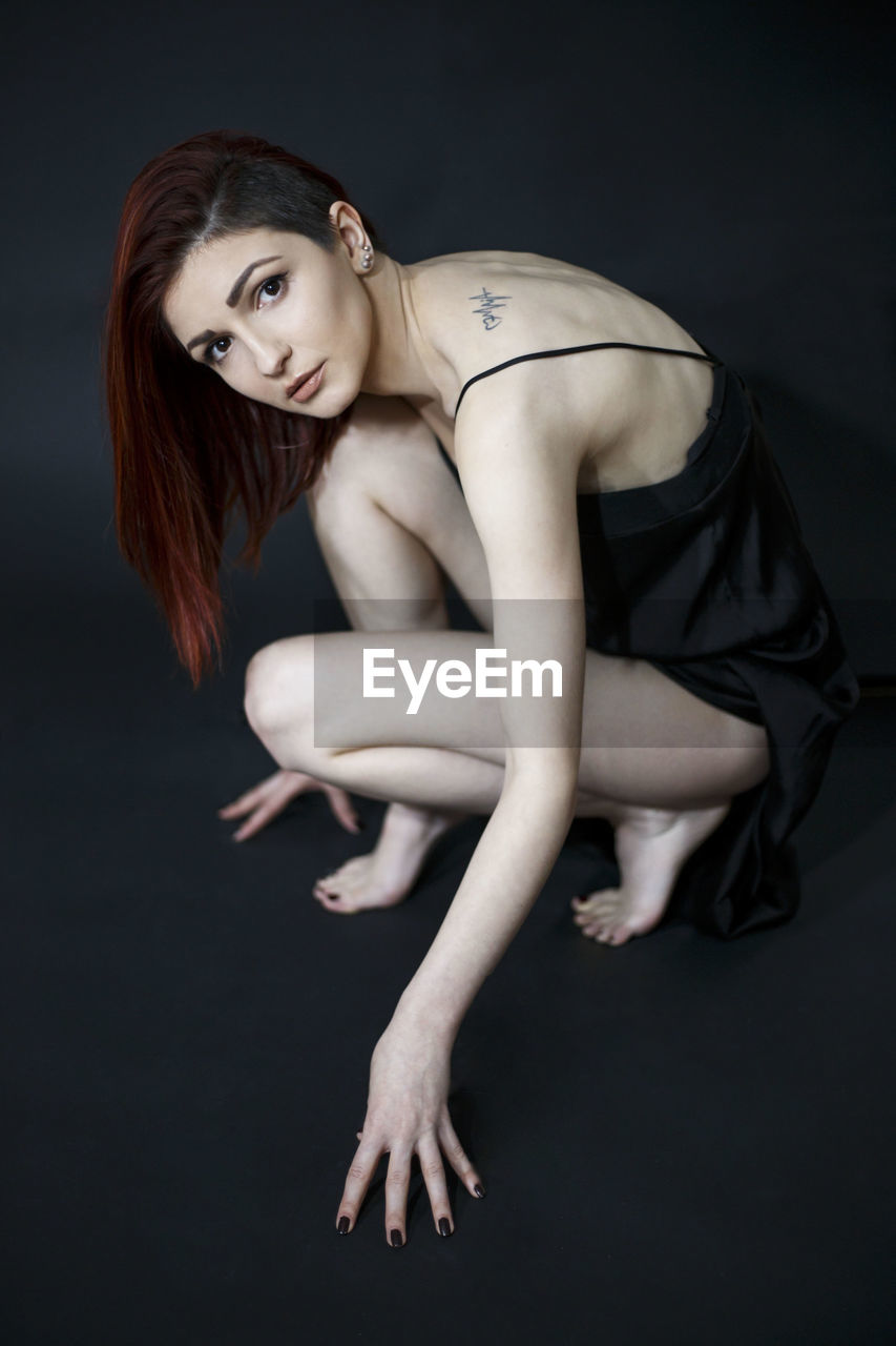 Side view portrait of beautiful young woman crouching over black background