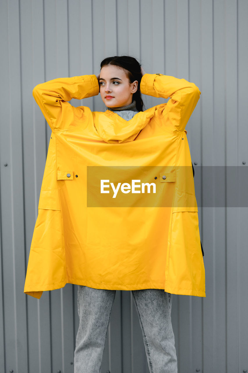 yellow, one person, outerwear, young adult, clothing, adult, sleeve, portrait, fashion, standing, women, three quarter length, raincoat, front view, orange, casual clothing, lifestyles, looking, looking at camera, indoors, brown hair, coat, leisure activity, jacket, emotion, collar