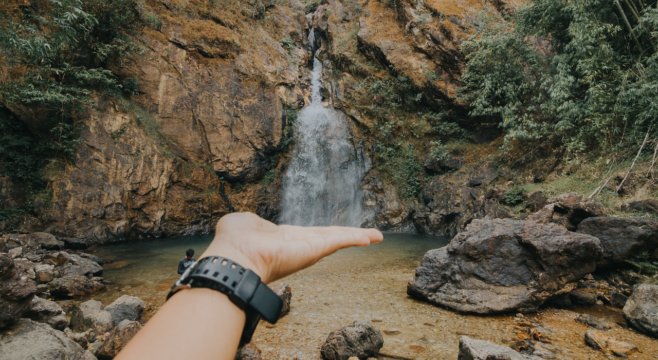 Optical illusion of young woman hand touching waterfall