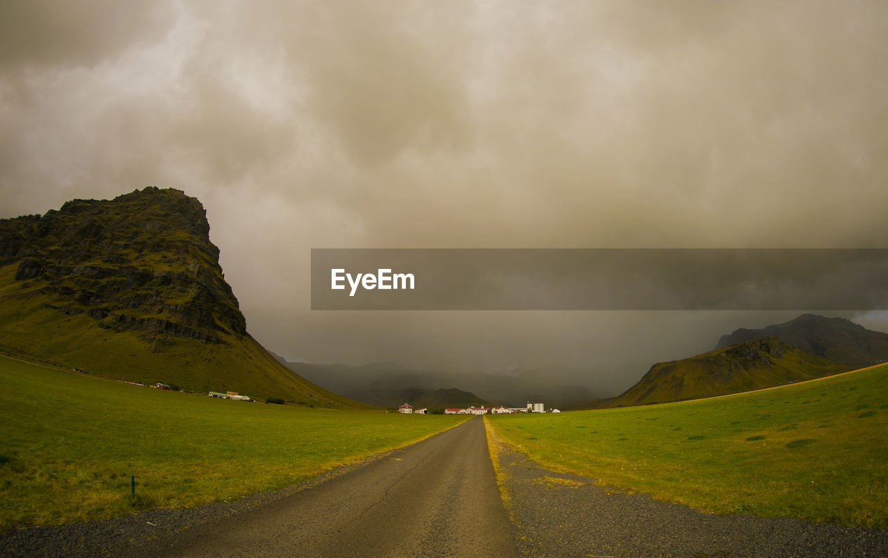 Empty road along landscape against cloudy sky