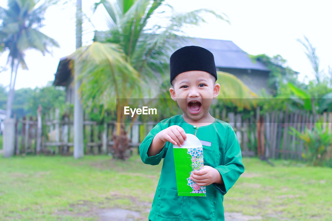 Portrait of smiling boy in traditional clothing holding envelope while standing on field