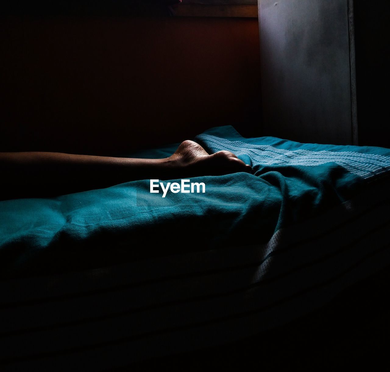Low section of person sleeping on bed in darkroom