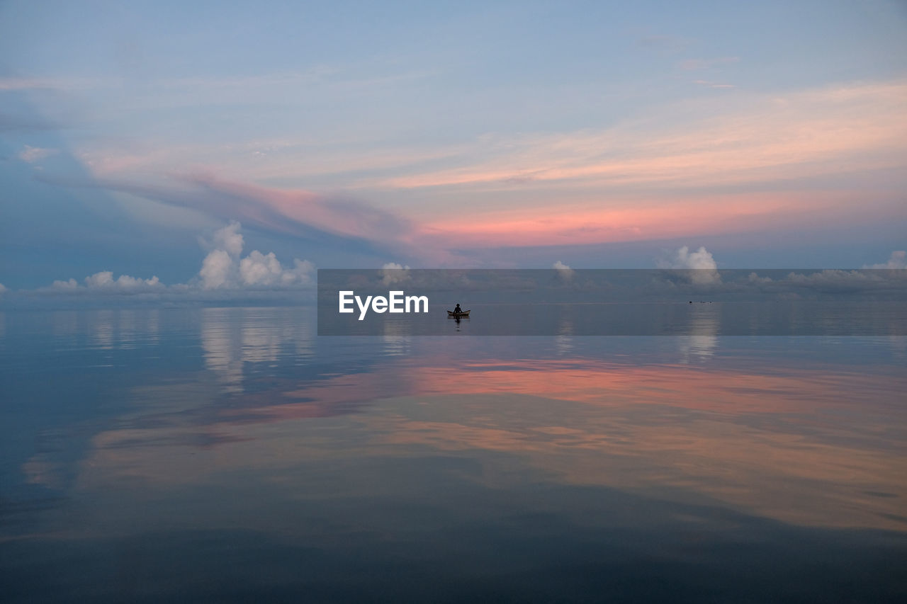 Small boat endless ocean of south pacific during sunset with dramatic clouds in the background