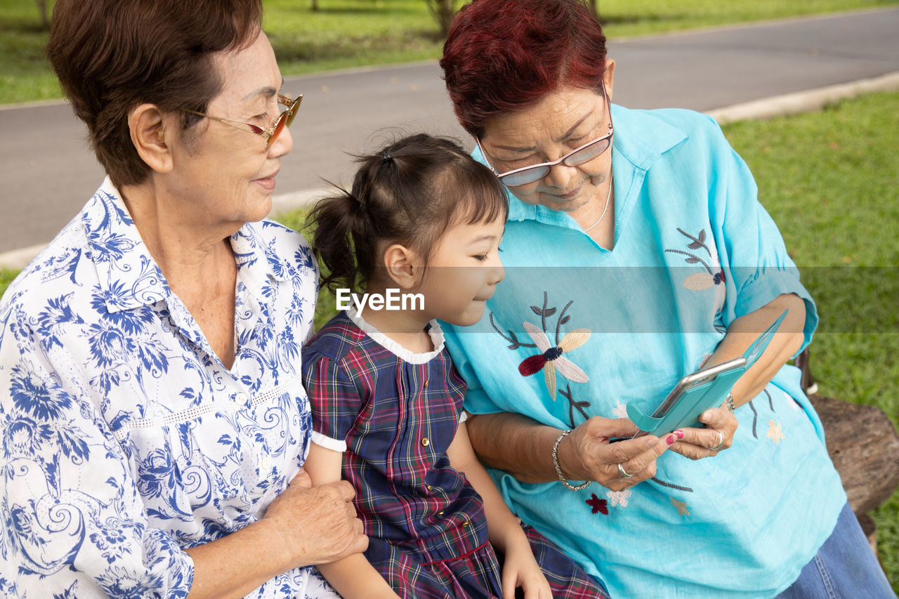 Grandmother showing smart phone to granddaughter at park