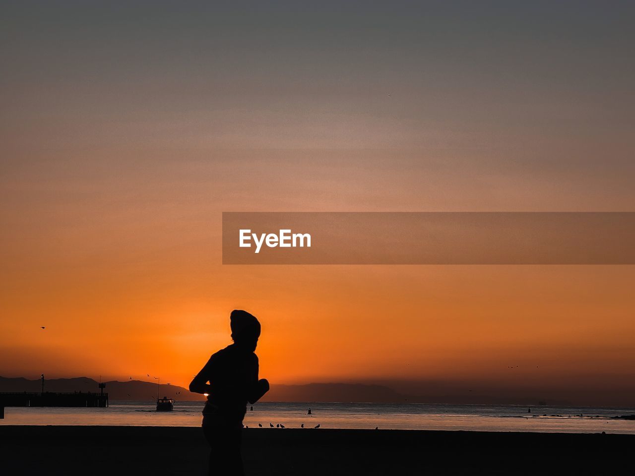 Silhouette woman standing on beach against sky during sunset