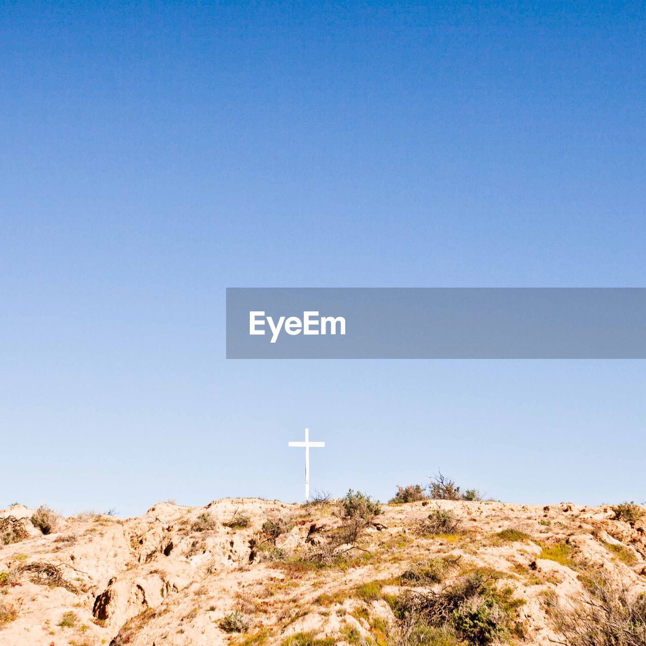 Low angle view of religious cross on rock against clear blue sky