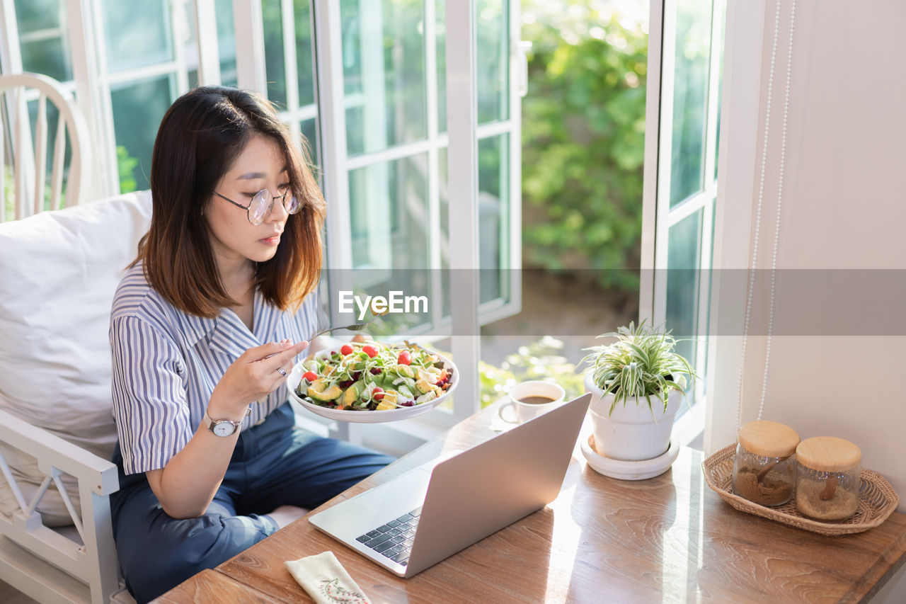 Businesswoman eating food while working on laptop at home