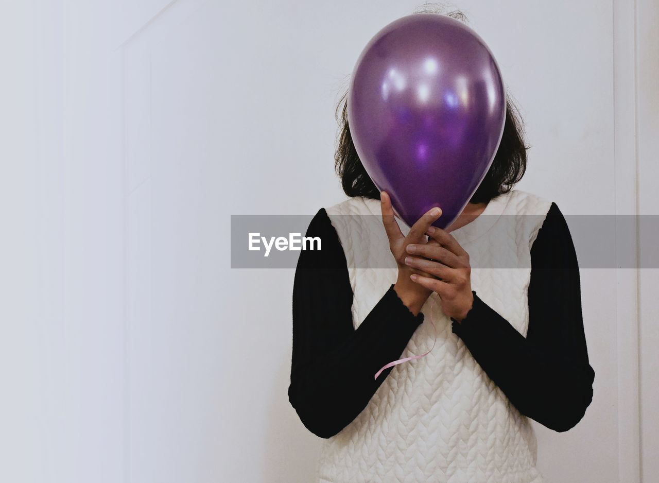 Woman covering face with balloon against wall