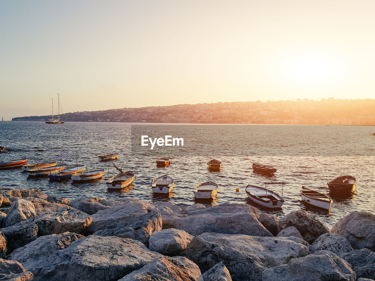 Boats moored in sea against sky at sunset