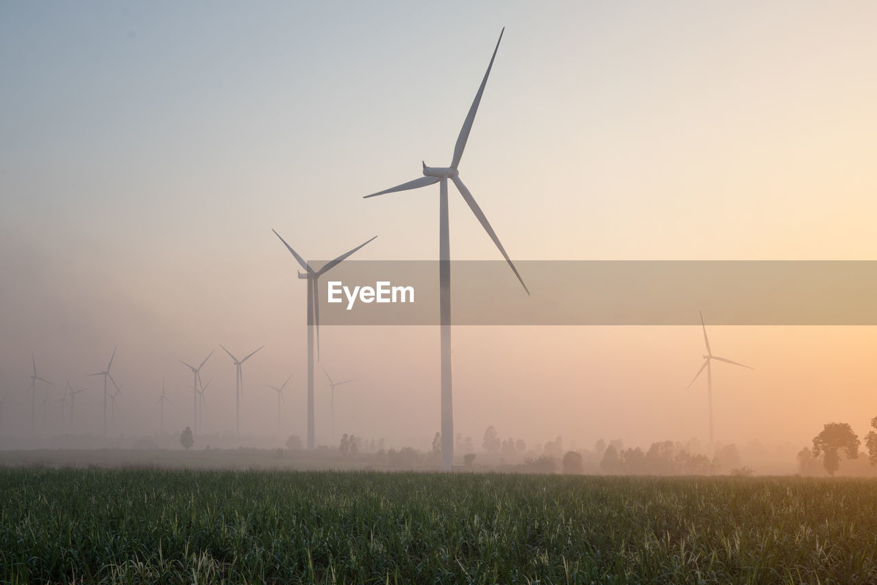 Wind turbines on field against sky during sunset
