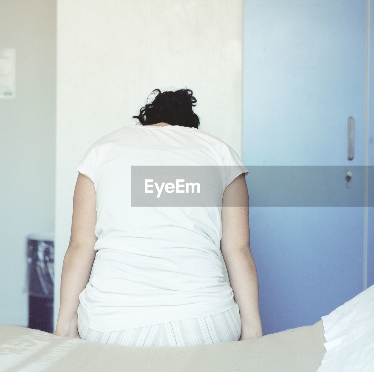 Rear view of woman sitting on bed at home