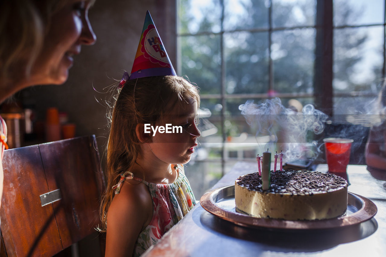 Girl looking at birthday cake with mother at home