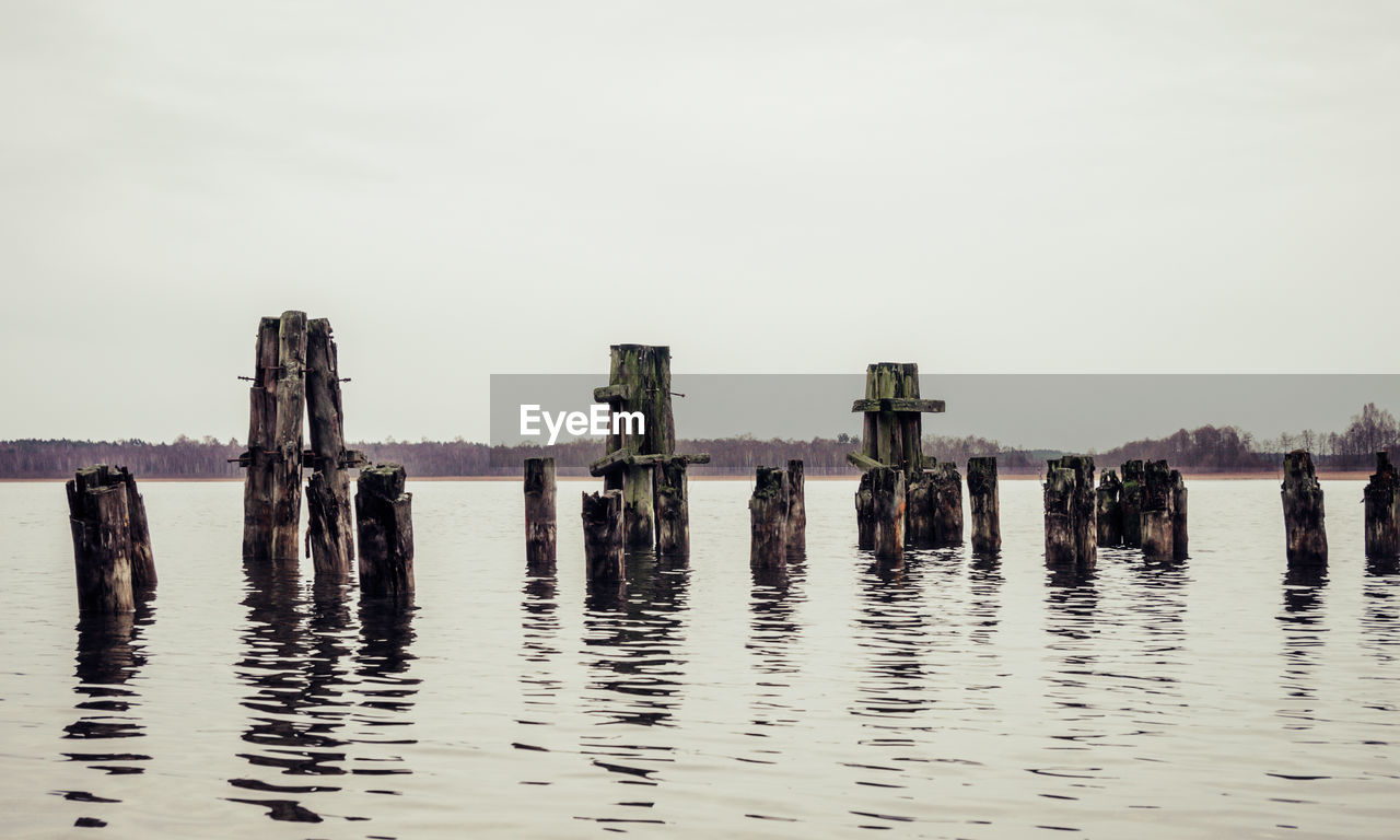 WOODEN POSTS IN CALM LAKE AGAINST CLEAR SKY