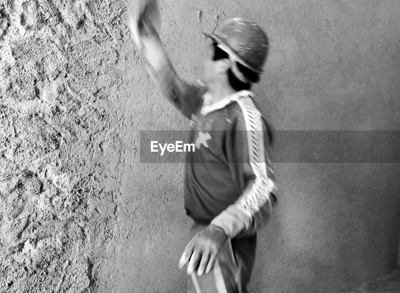 SIDE VIEW OF A WOMAN WITH ARMS OUTSTRETCHED STANDING AGAINST WALL