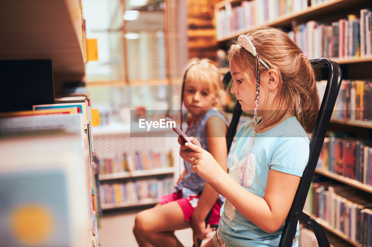 Schoolgirls looking for books in school library. students choosing books. elementary education