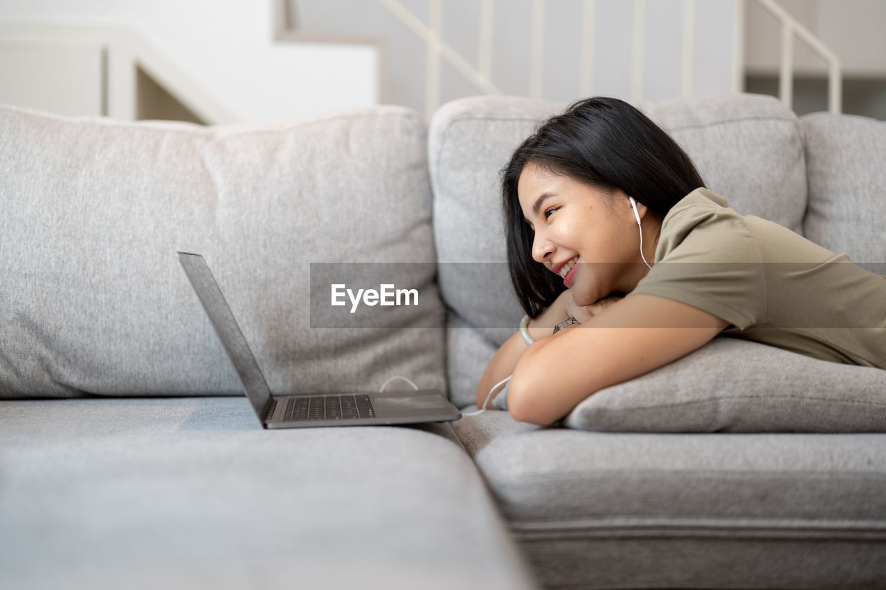 portrait of young woman using laptop while sitting on sofa at home