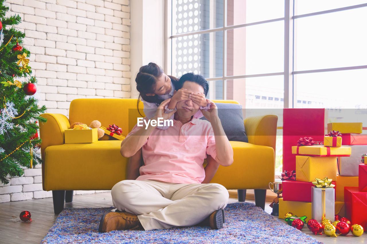 Cute girl covering eyes of father while sitting on sofa at home