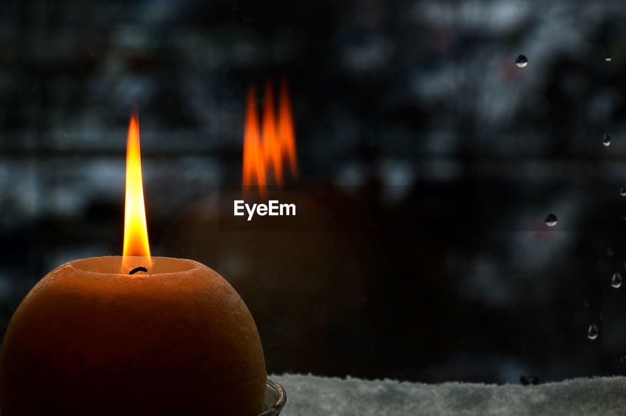 Close-up of burning candle by window