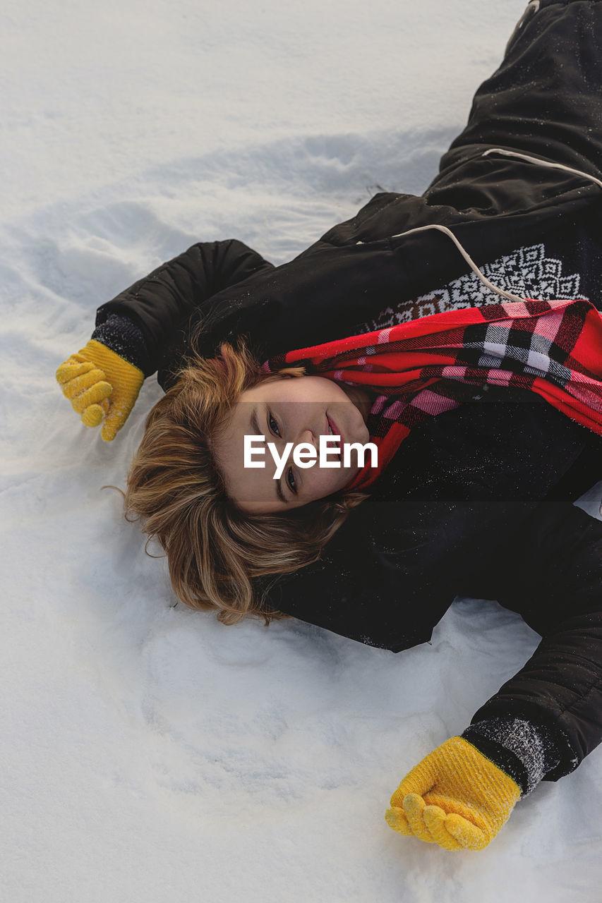 Blonde caucasian girl with red scarf lies on the snow enjoying winter. happy joyful winter concept