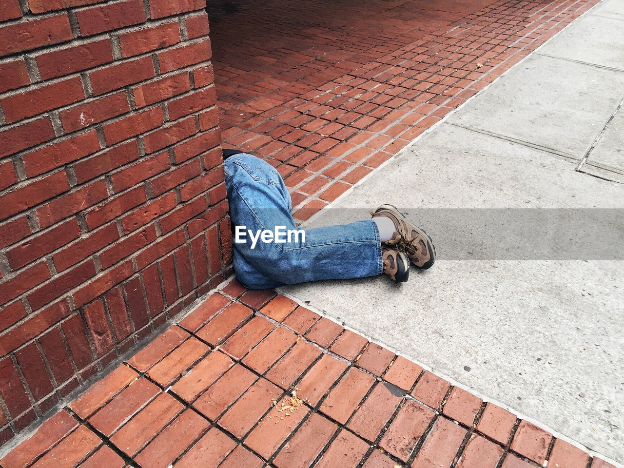 Low section of person sleeping by brick wall