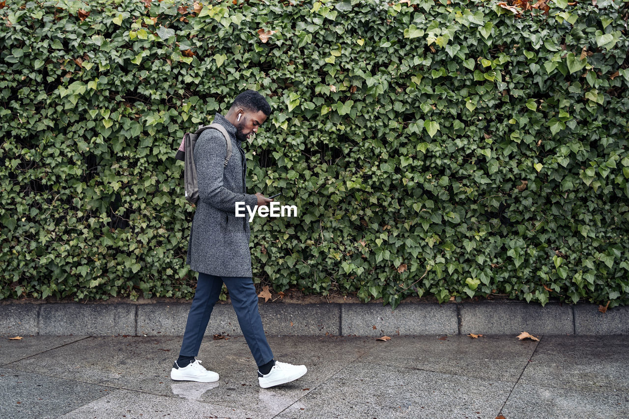 Side view of man walking on footpath against plants