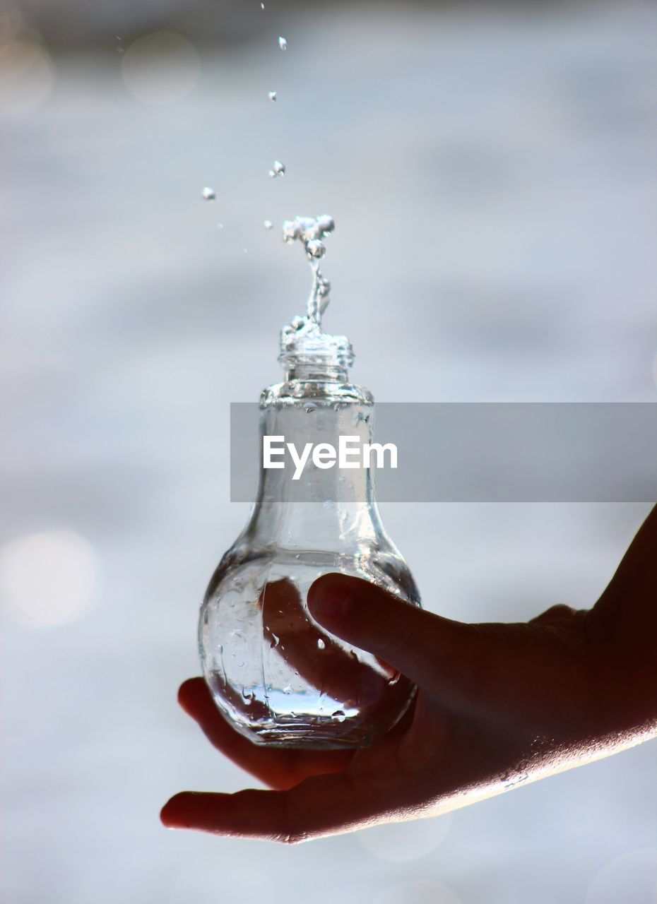 Cropped hand holding drinking water in glass bottle