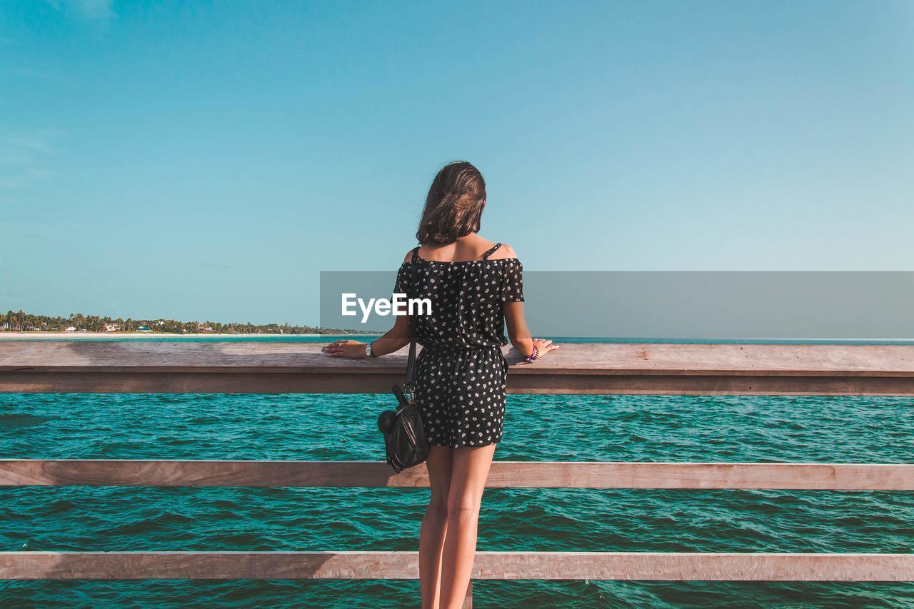 REAR VIEW OF WOMAN STANDING AGAINST SEA