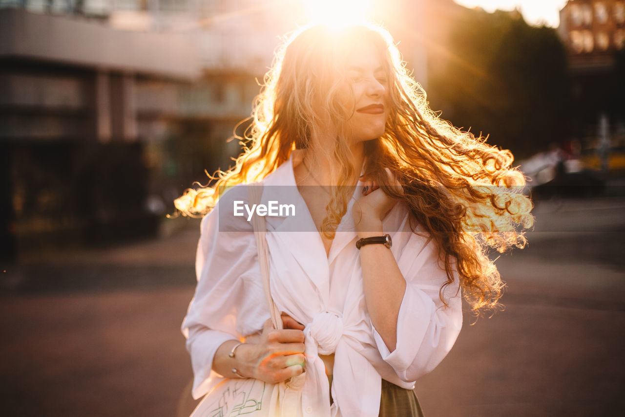 Portrait of happy successful woman with tousled hair in city at sunset