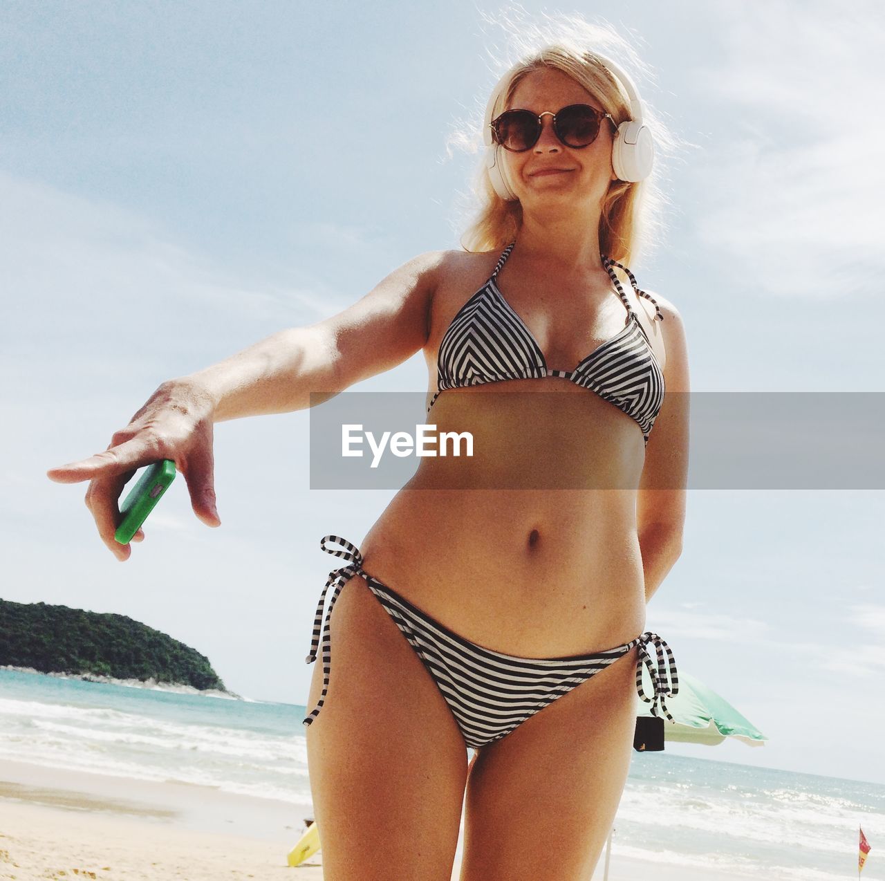 Woman wearing sunglasses standing at beach against sky