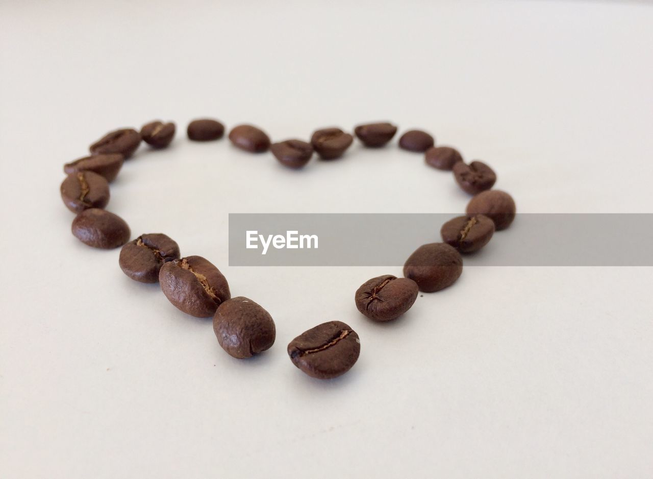 Close-up of coffee beans in heart shape against white background