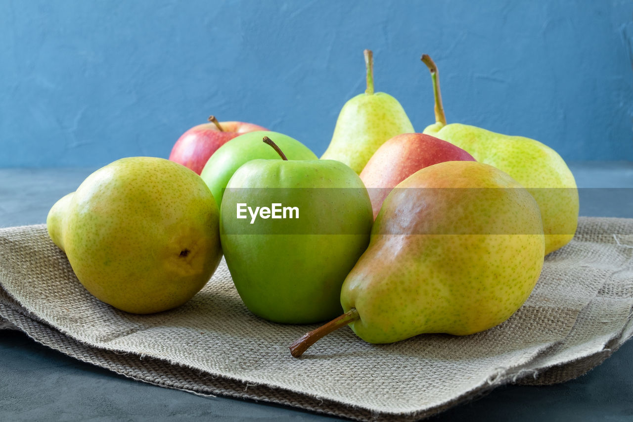 A few fresh bright apples and pears lie on a simple coarse rustic napkin on a blue background.