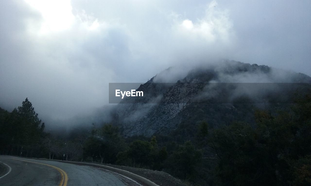 Empty road passing through landscape against cloudy sky