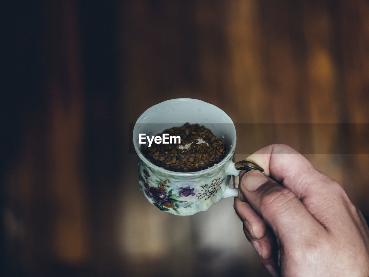 Close-up of hand holding coffee cup against wooden floor - retro edit