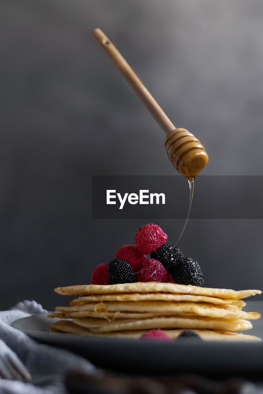 Levitating honey dipper pouring raw honey over homemade crepes on table, dark food photography