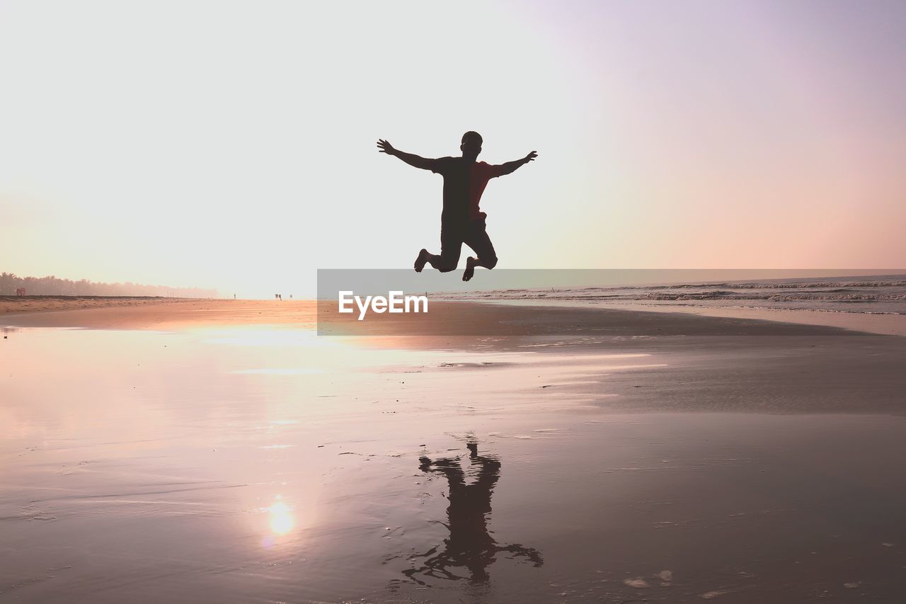 Man jumping at beach against sky during sunset