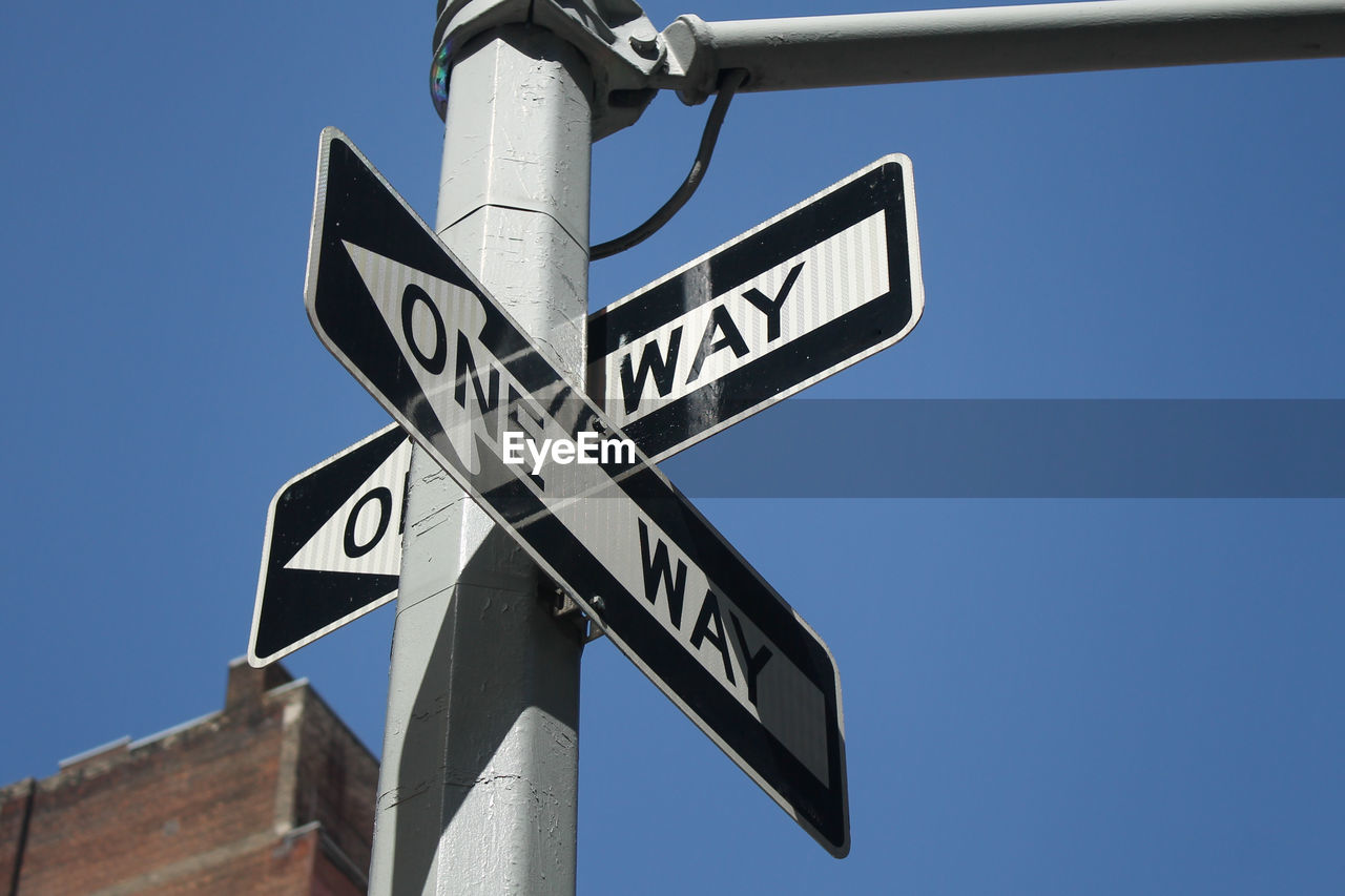 Low angle view of one way sign against clear blue sky