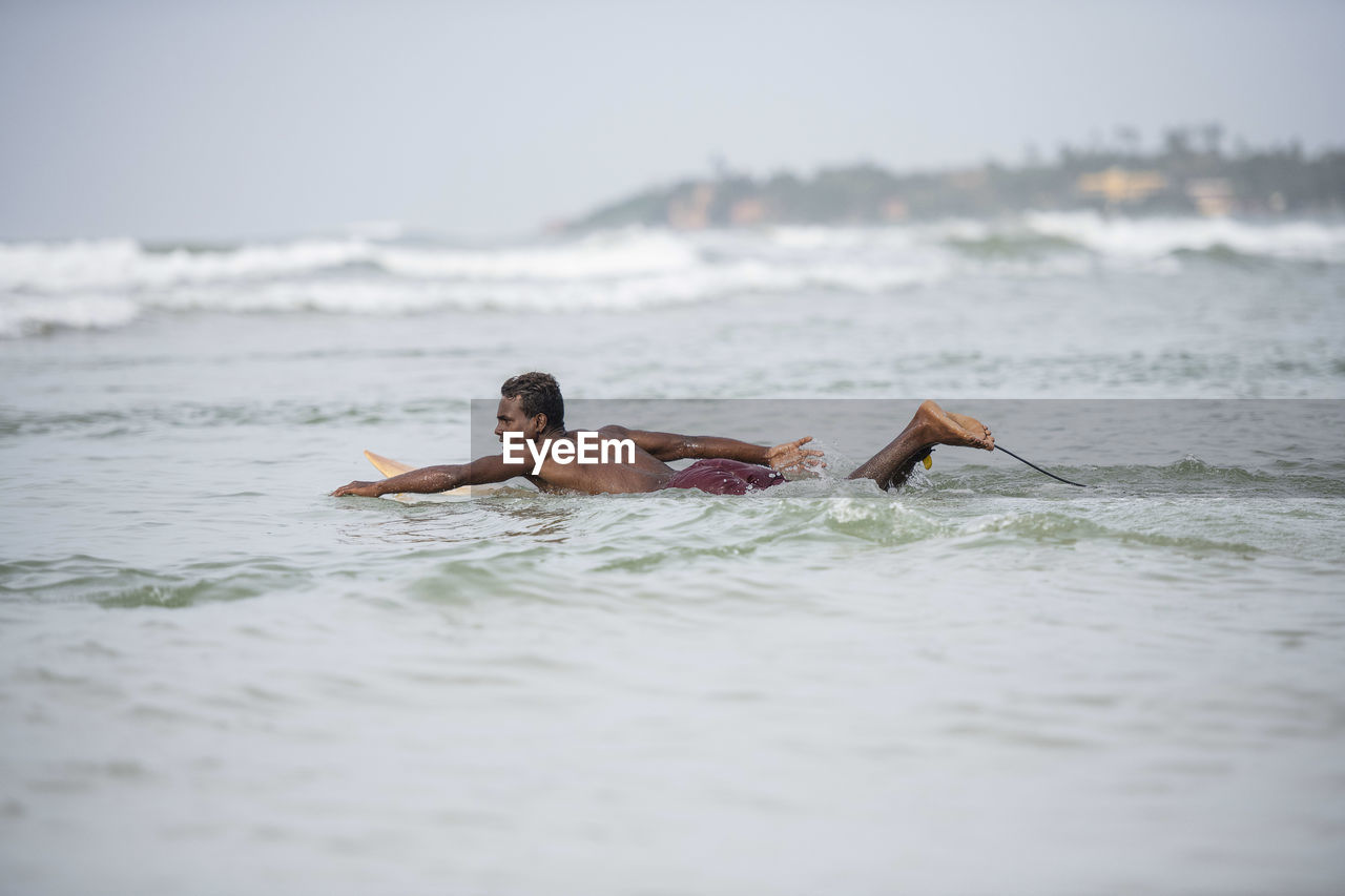 Shirtless man surfing in sea against sky