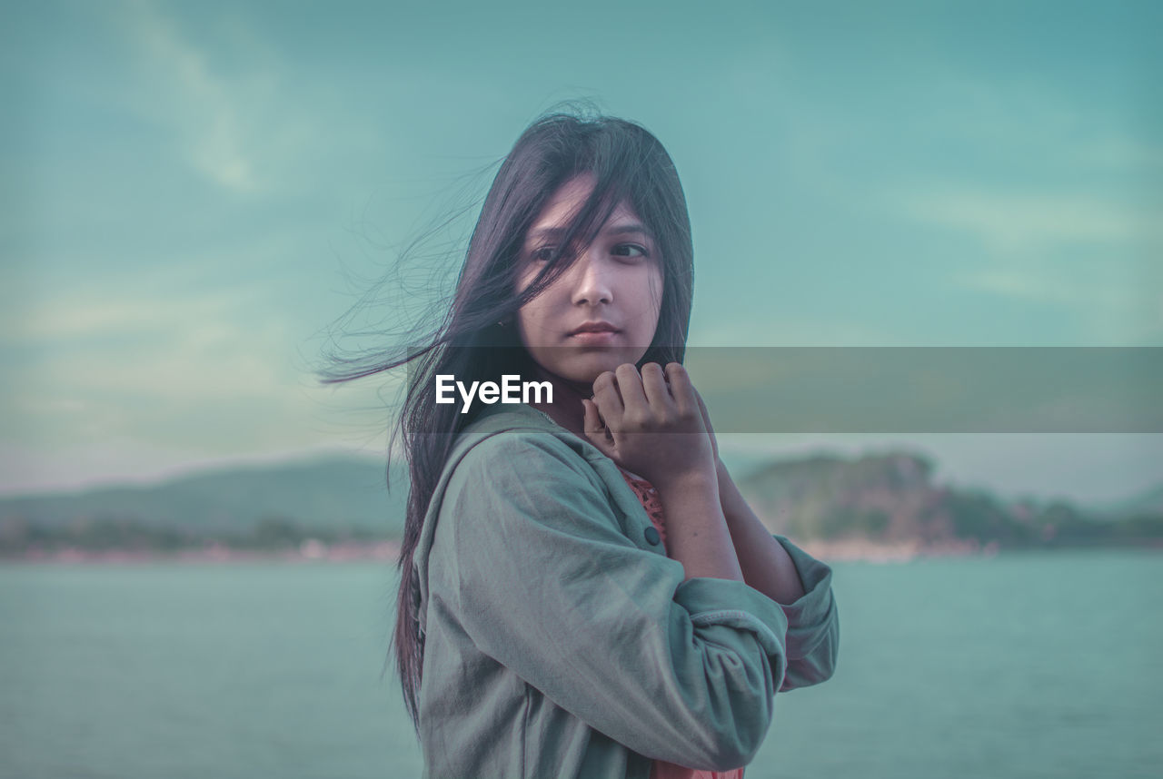 PORTRAIT OF BEAUTIFUL YOUNG WOMAN STANDING AGAINST LAKE