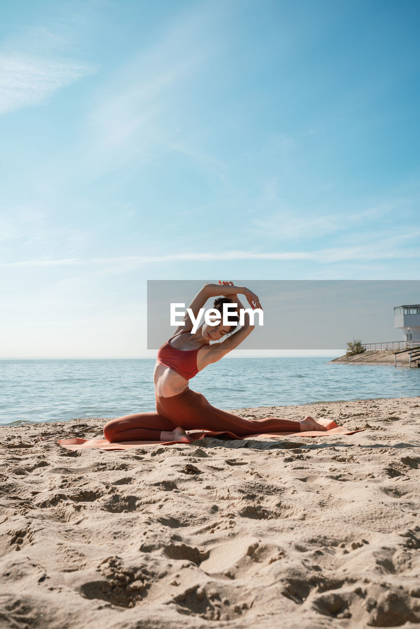 Full length of woman exercising on beach against sky