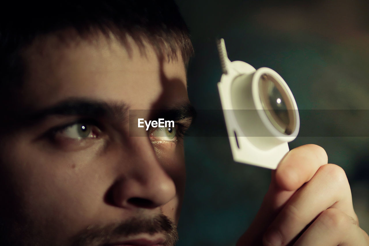 Close-up of young man's eyes holding a magnifying glass 