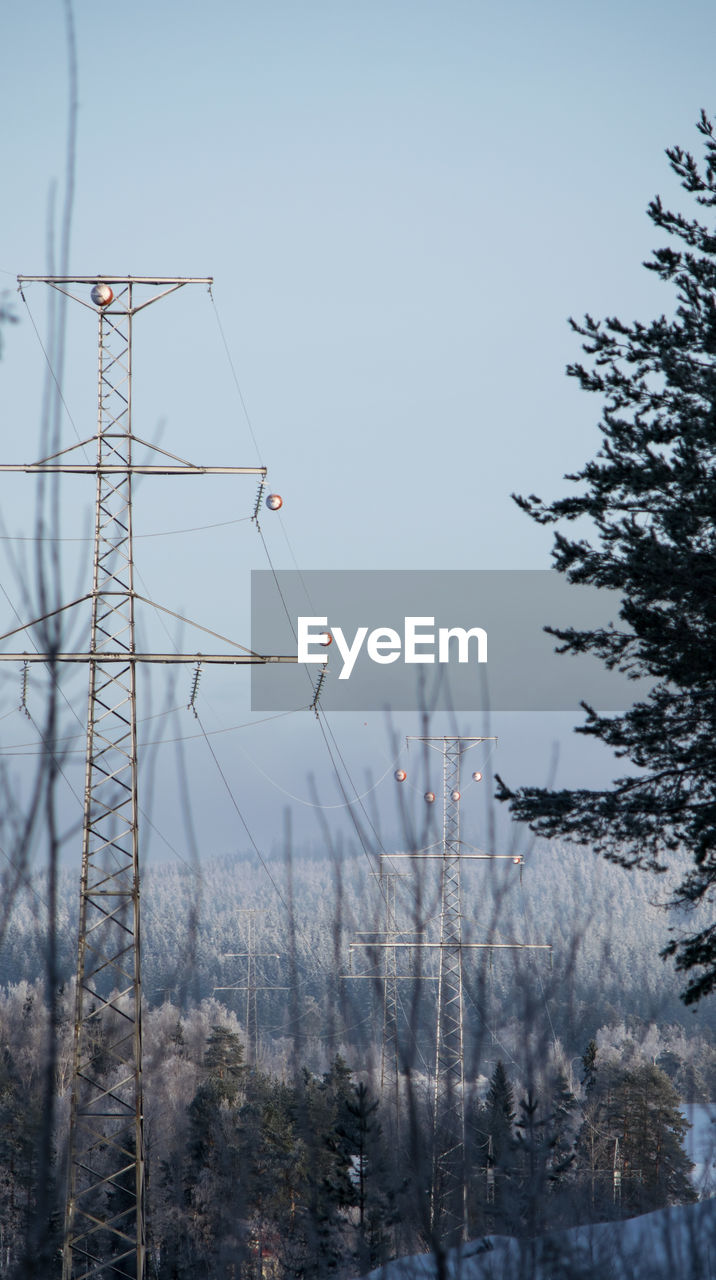 Low angle view of electricity pylons and trees against clear sky