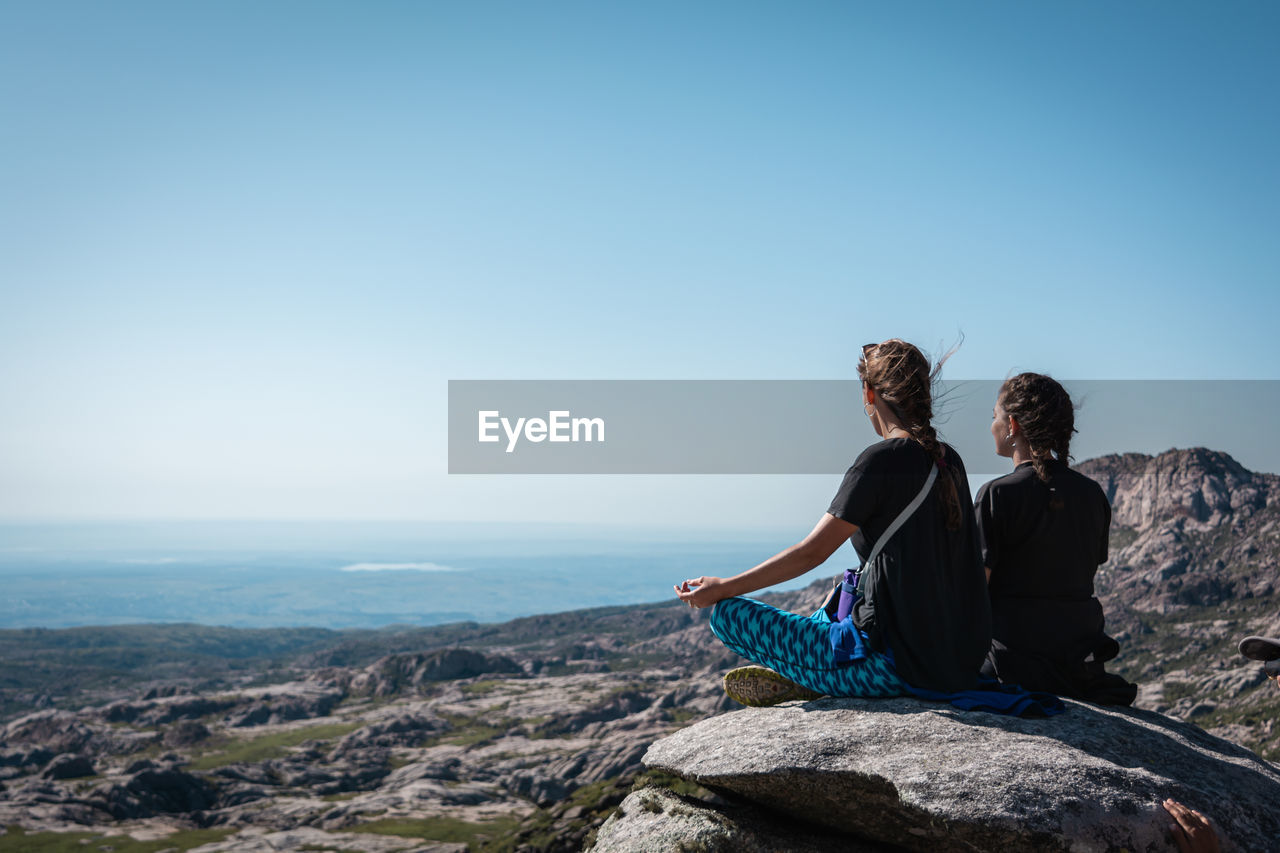 Rear view of people sitting on rock looking at view