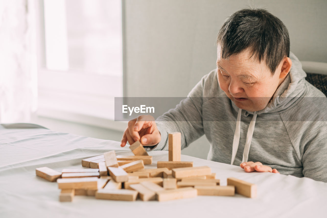 Elderly woman with down syndrome and an asian girl play in tower from wooden blocks