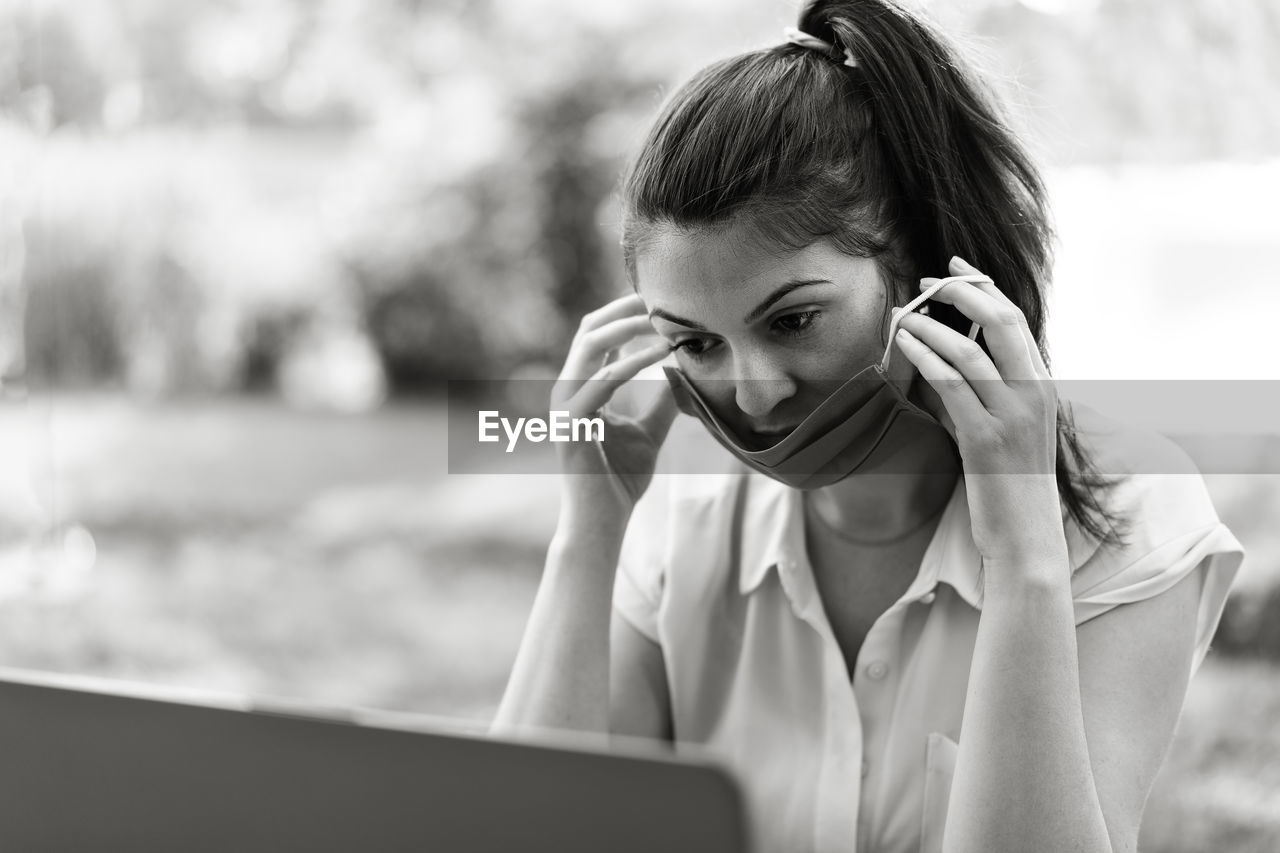 Woman wearing mask while looking at laptop at park