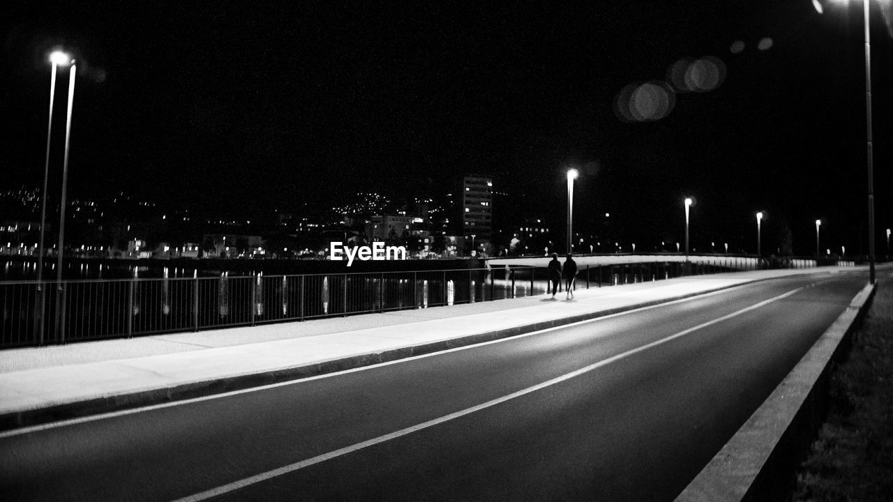 EMPTY ROAD ALONG ILLUMINATED STREET LIGHTS