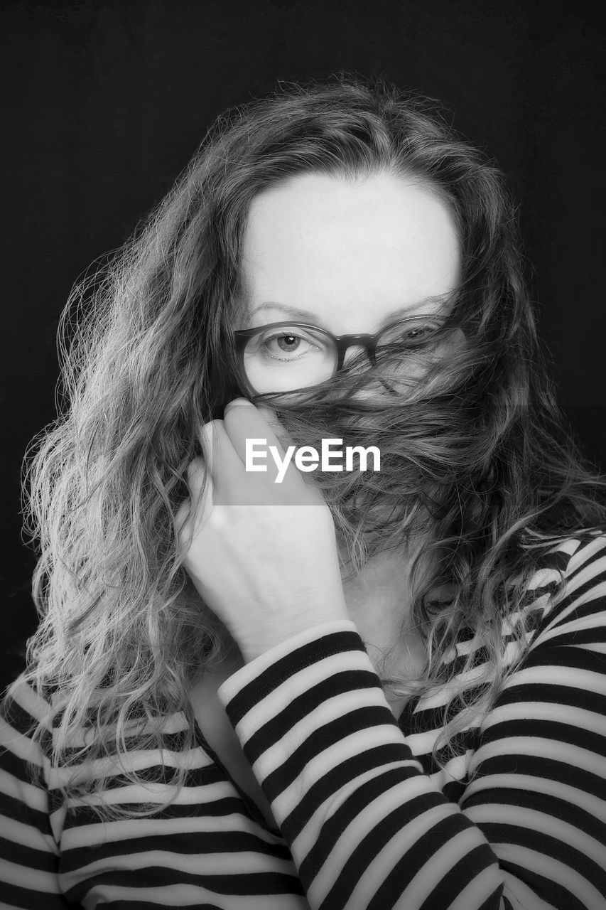 Woman covering face with hair in front of black background 