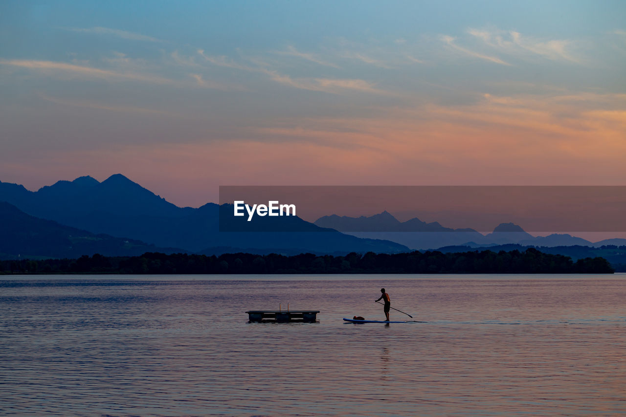 Man paddleboarding on lake against sky during sunset