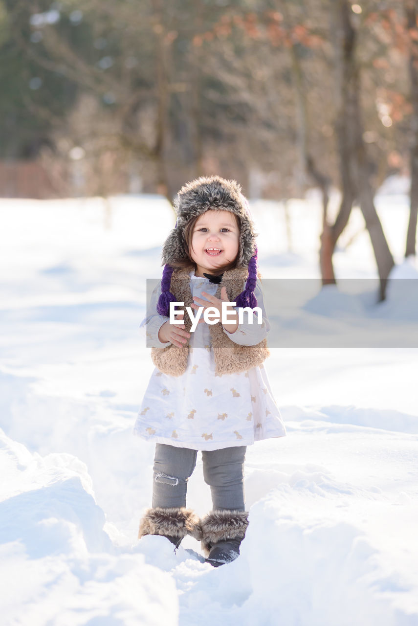 Portrait of happy girl standing on snow covered field