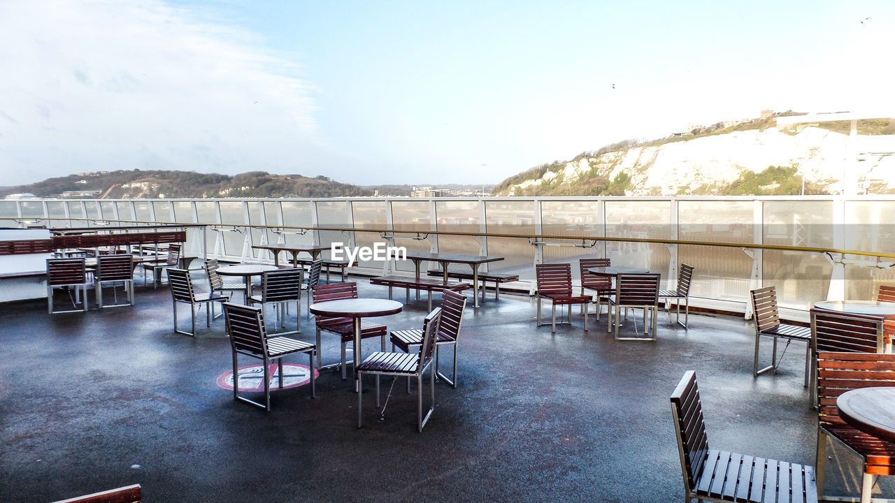 EMPTY CHAIRS AND TABLES AGAINST SKY ON WATER